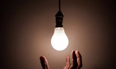 Mano alcanzando una bombilla encendida en una habitación oscura.