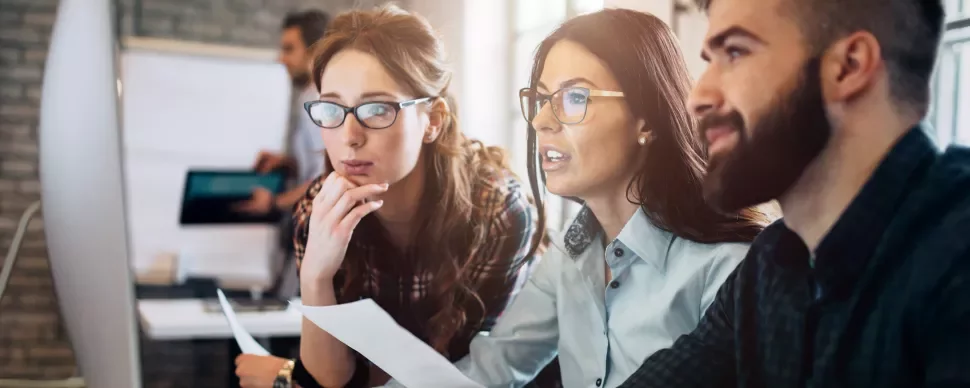 Tres personas discuten frente a un monitor en una oficina moderna.