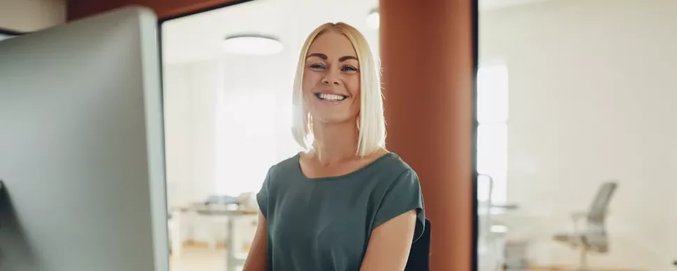 Persona sonriendo frente a una computadora en una oficina iluminada.