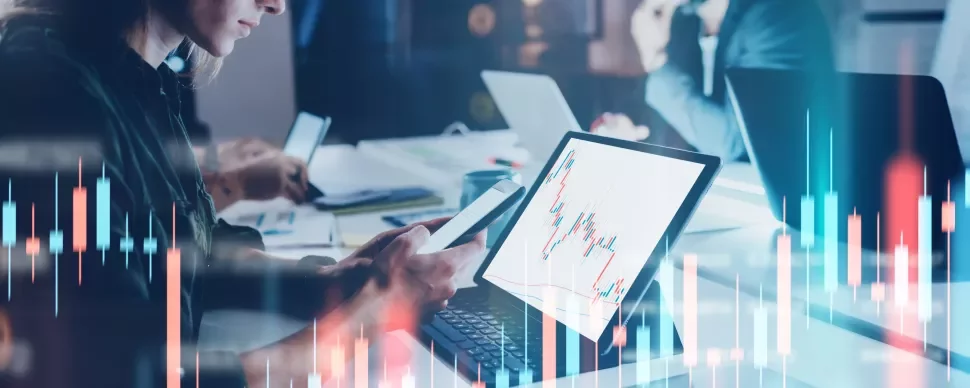 Personas trabajando en laptops con gráficos de datos en pantalla.
