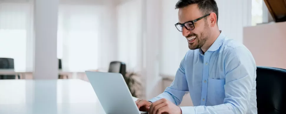 Persona sonriendo mientras usa una computadora portátil en una oficina.
