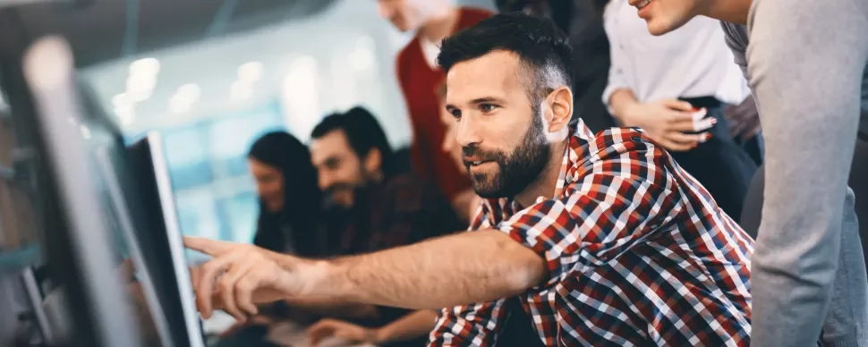 Personas colaborando frente a una computadora en una oficina moderna.