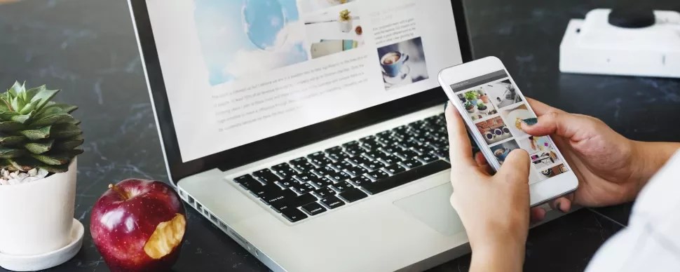 Persona usando un teléfono y una laptop en una mesa con una manzana y suculenta.