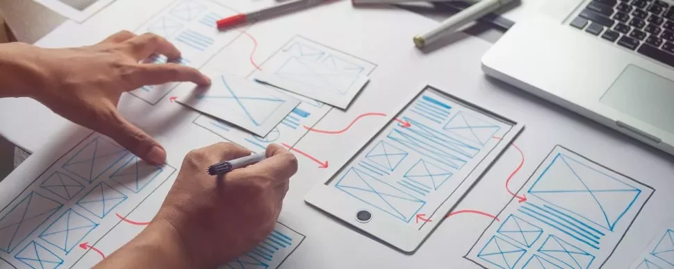 Persona diseñando una aplicación móvil con bocetos en papel.