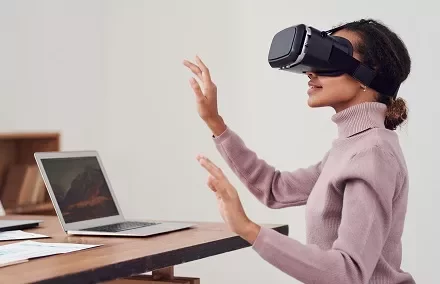 Persona usando una realidad virtual mientras está sentada frente a una computadora portátil.