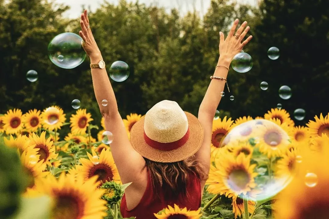 Persona entre girasoles, brazos alzados y burbujas alrededor.