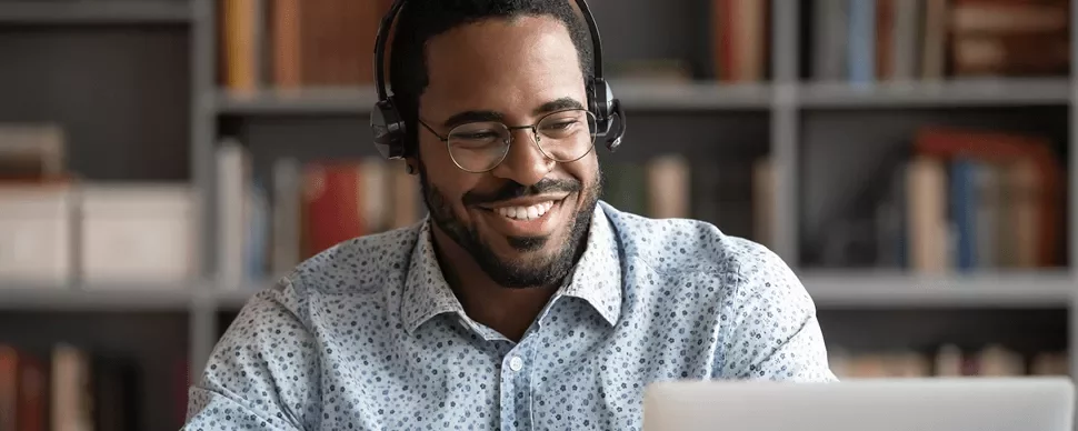 Persona con auriculares sonríe frente a una computadora portátil.