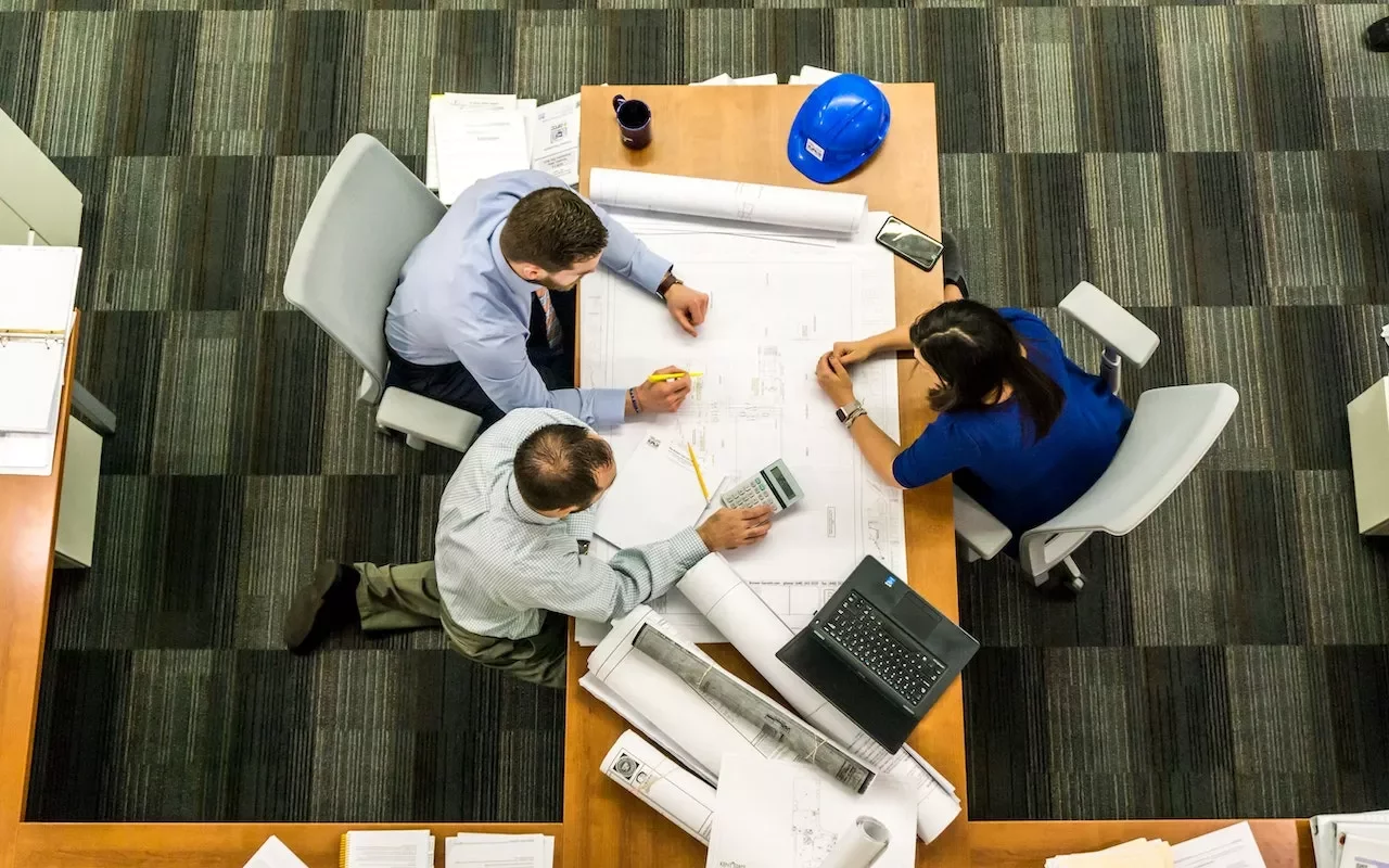 Tres personas revisan planos en una sala de reuniones.