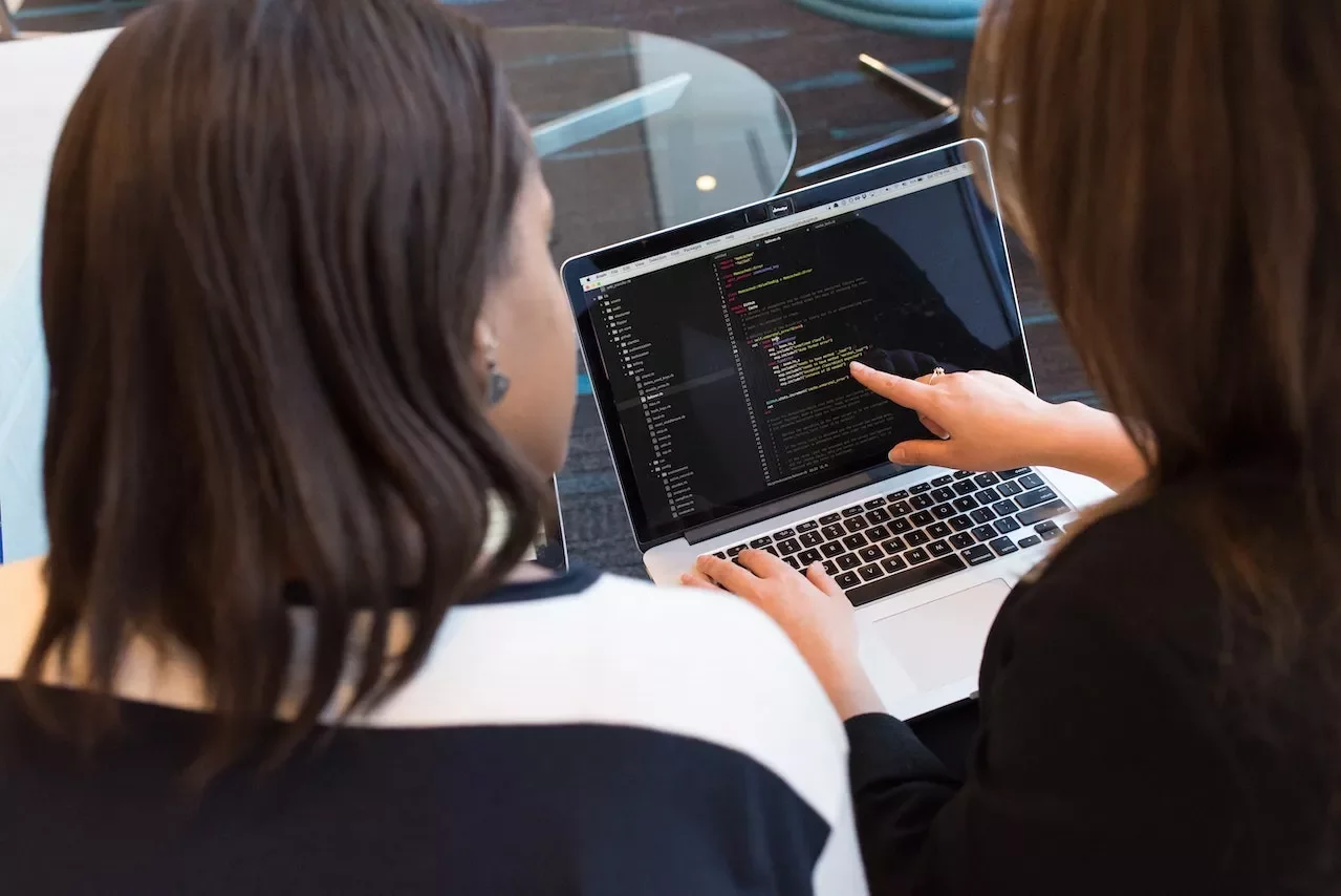Dos personas revisan código en una computadora portátil.