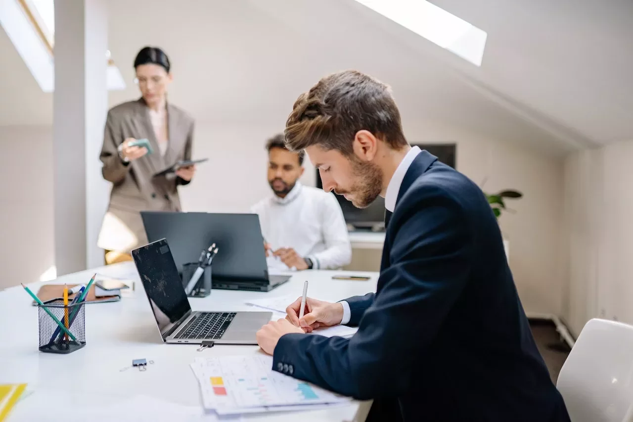 Personas trabajando en una oficina con portátiles y papeles.