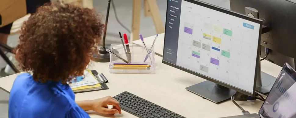 Persona trabajando en un escritorio con una computadora mostrando un calendario.