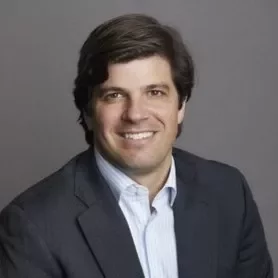 Una persona sonriente con ropa formal sobre un fondo gris.