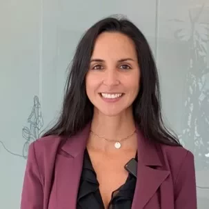 Persona sonriendo en una oficina con chaqueta púrpura.