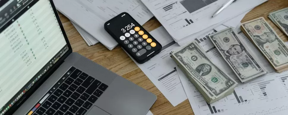 Imagen de una mesa con notas, ordenador, calculadora y billetes