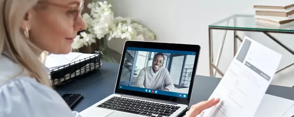 Mujer haciendo una entrevista de trabajo online mirando el CV del candidato que aparece en la pantalla de su ordenador