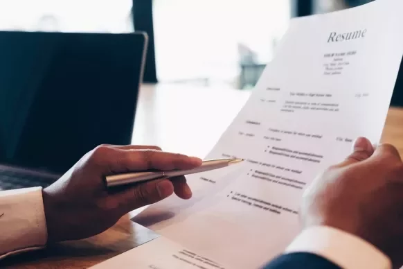 Manos revisando un currículum en una oficina.