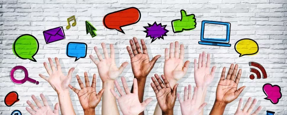 manos de diferentes colores alzadas e iconos de conversación dibujados en una pared blanca