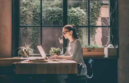 Persona con gafas trabajando en una computadora portátil junto a una ventana.