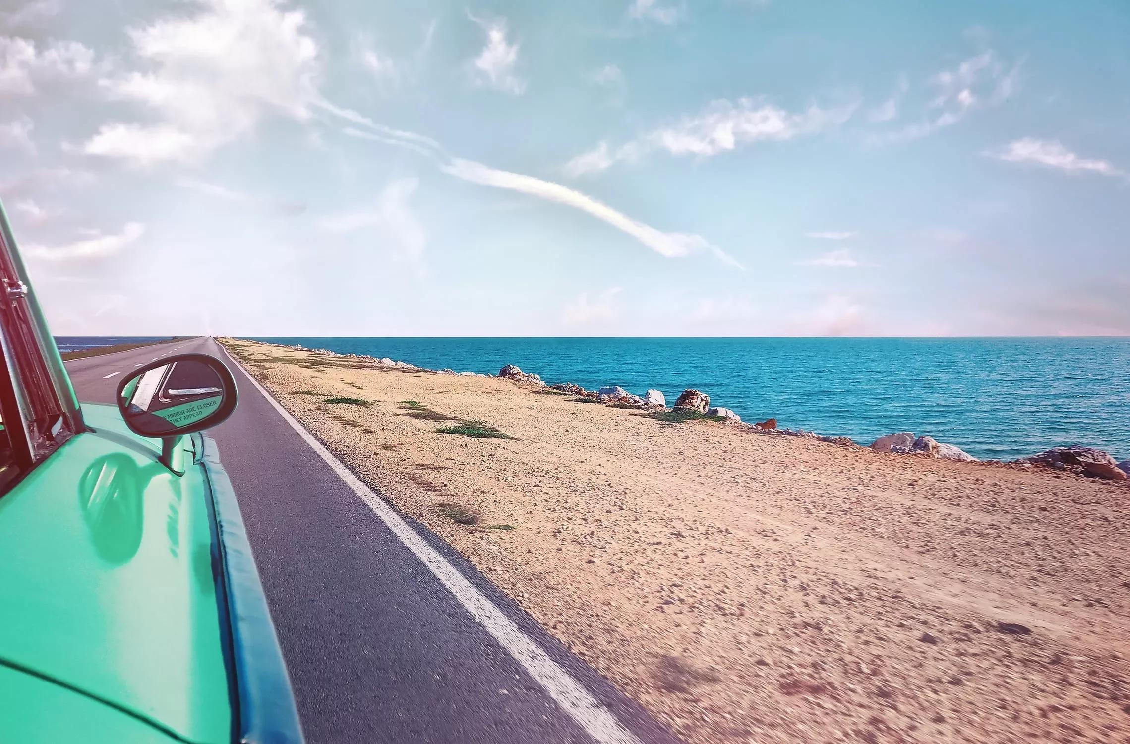 Un coche verde en una carretera junto al mar.