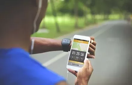 Persona usando una aplicación de ejercicio en el teléfono y un reloj inteligente en un camino.
