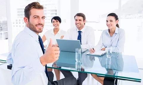 Un grupo de personas en una reunión de negocios, con una persona mostrando un pulgar arriba.