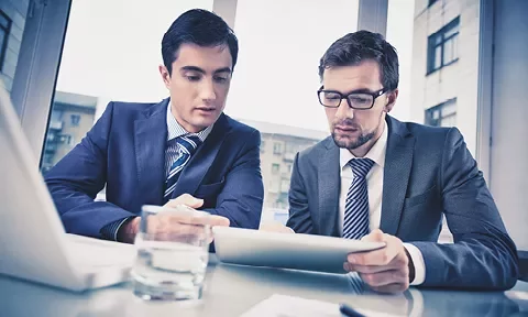 Dos personas en trajes revisan un documento en una oficina.