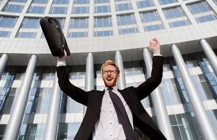 Persona vestida formalmente celebrando frente a un edificio de oficinas.