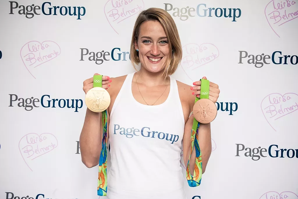 Persona mostrando dos medallas olímpicas frente al fondo Michael Page.
