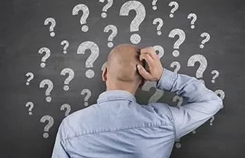 Persona rascándose la cabeza frente a una pizarra con signos de interrogación.