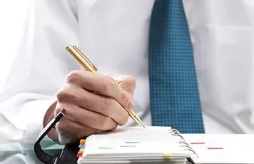 Persona usando una pluma dorada para escribir en una agenda.
