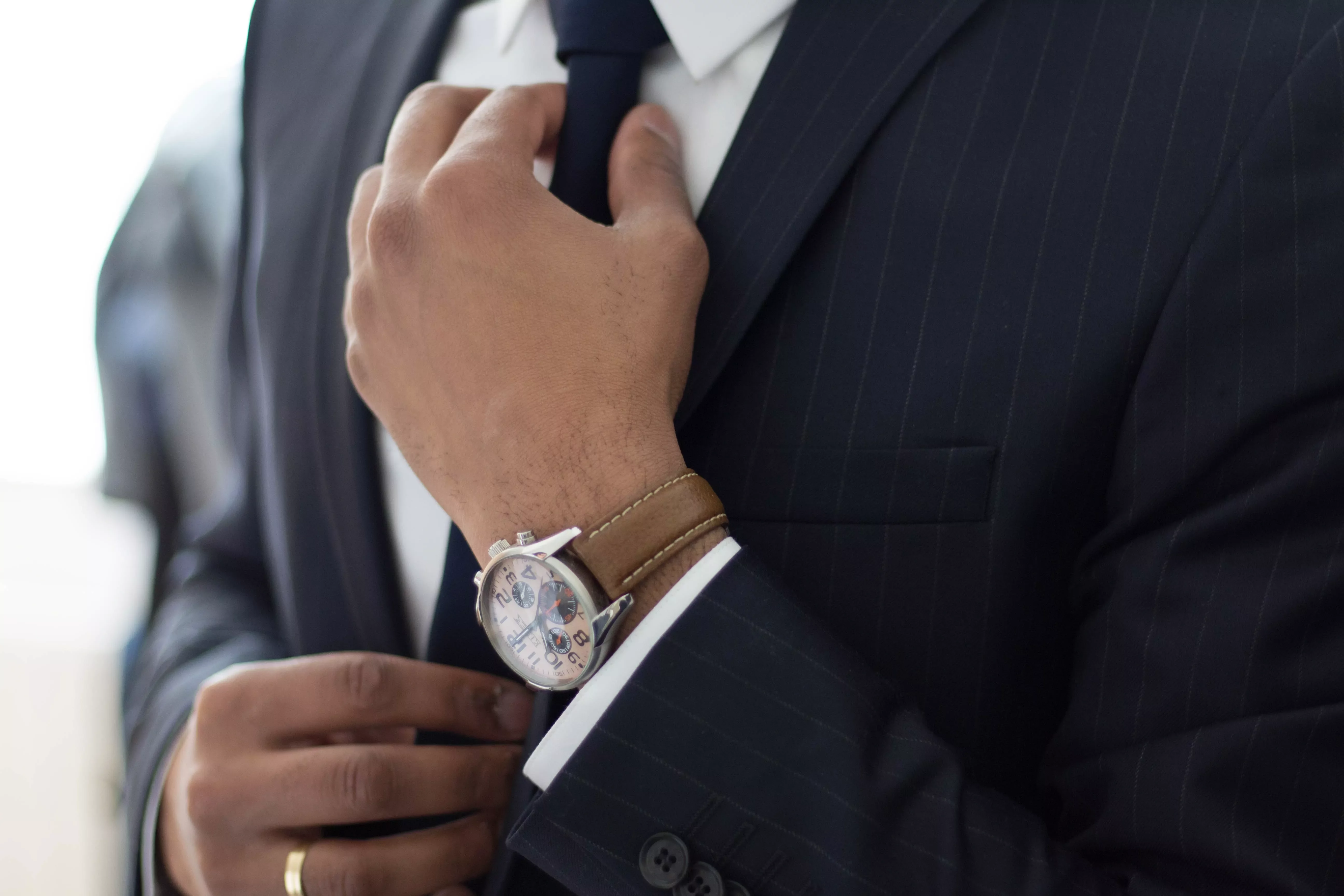 Persona ajustando una corbata y llevando reloj mientras lleva un traje.
