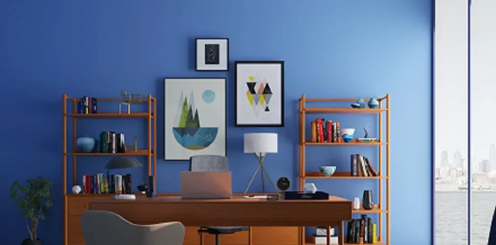 Una oficina con escritorio de madera y estantes llenos de libros, contra una pared azul con arte.
