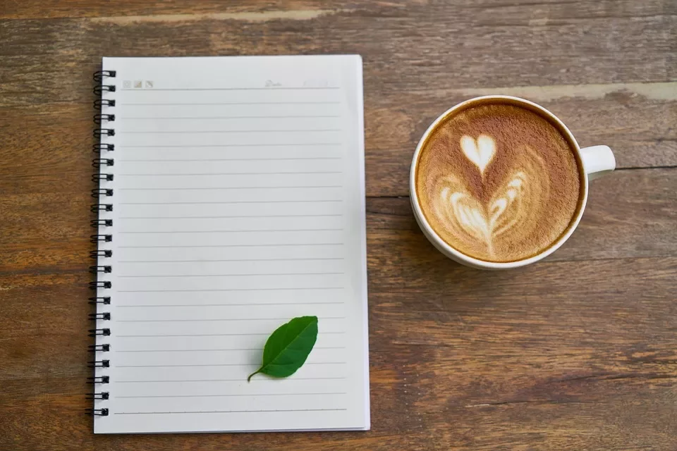 Taza de café con latte arte y cuaderno sobre mesa de madera