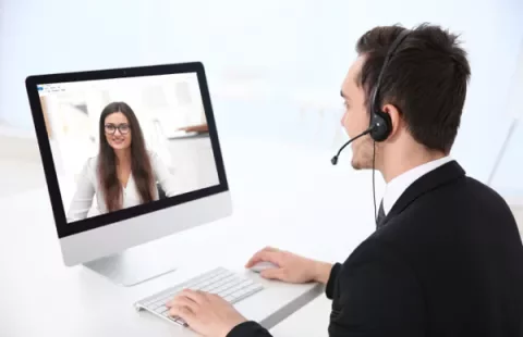 Persona en videollamada con auriculares, trabajando frente a un ordenador.