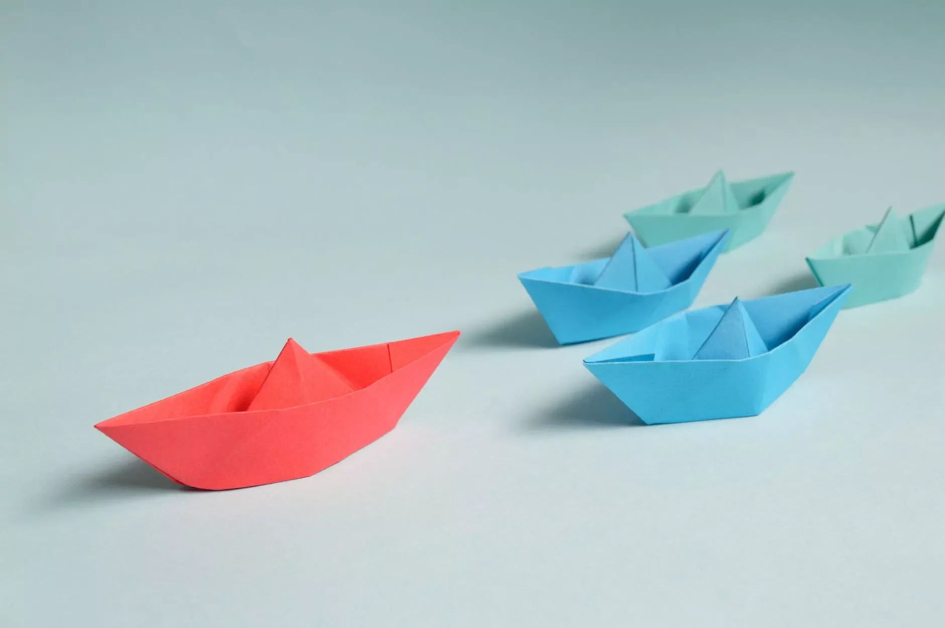 Botes de papel en fila, uno rojo y otros azules.