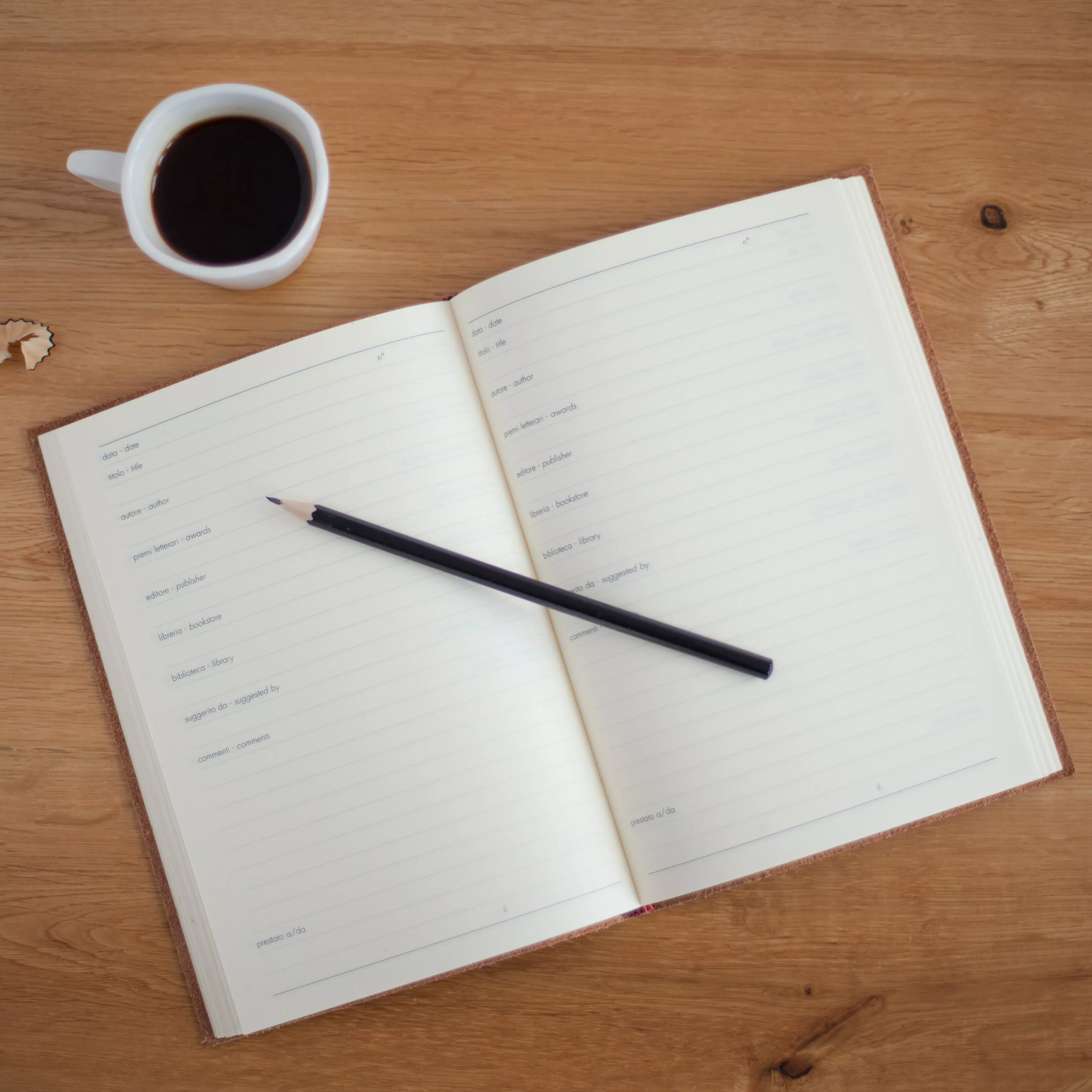 Un cuaderno abierto con un lápiz negro y una taza de café en una mesa de madera.